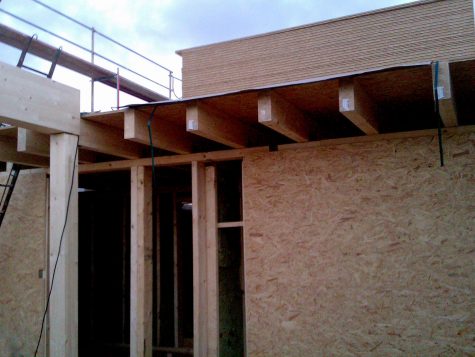 Vista de una casa de madera en construcción donde puede verse parte de la estructura y una pared
